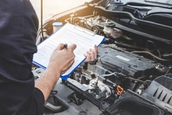 Services car engine machine concept, Automobile mechanic repairman checking a car engine with inspecting writing to the clipboard the checklist for repair machine, car service and maintenance.