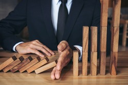 Close up of businessman hand Stopping Falling wooden Dominoes effect from continuous toppled or risk, strategy and successful intervention concept for business.