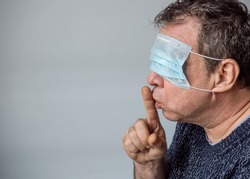 A man in a medical mask put a finger to his lips. Coronavirus conspiracy thesis concept