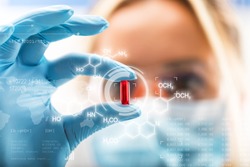Young attractive female scientist holding a red transparent pill with futuristic scientific air interface with chemical formulas and research data in the foreground