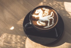 Hot coffee latte with latte art in the form of a horse milk foam in cup mug on wood desk on top view. As breakfast In a coffee shop at the cafe,during business work concept