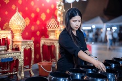 Asian woman tourist Make merit by dropping coins into the alms bowl. to Buddha for worship with faith to Buddha statue in temple thailand belief in Buddhism