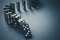 Black dominoes chain on a dark table background. Domino effect concept