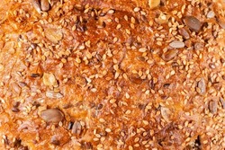 Background, texture of baked crust of healthy whole wheat bread of round shape with the addition of sesame seeds, sunflower, flax, pumpkin. Proper nutrition. Sourdough bread.