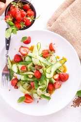 light summer detox salad with strawberries, cucumber, nuts and flax seeds on white plate