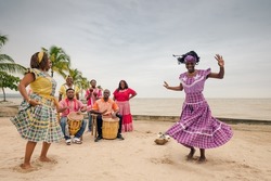 Two beautiful black women dance on a Caribbean beach, accompanied by a local musical group.