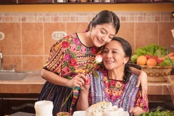 Mother receives a rose from her daughter for Mother's Day, happy mother in the kitchen of her house.