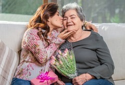 Happy Mother's Day! Hispanic mom and daughter kiss, hug and give each other flowers and gifts on a special day.