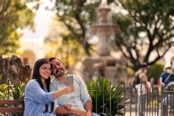 Young tourists are enjoying their vacations in the colonial city.
 Hispanic couple tourists take a selfie with their cell phones in the park.