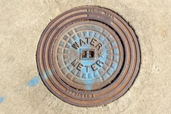 Circular Water Meter placed in a sidewalk.