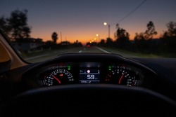 Driver view to the speedometer at 59 kmh or 59 mph, on a road blurred in motion, night fall view from inside a car of driver POV of the road landscape.