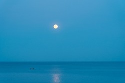 The full moon rises over the sea at a colorful sunset. Fisherman boat in the sea.