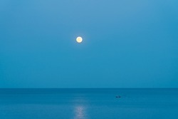 The full moon rises over the sea at a colorful sunset. Fisherman boat in the sea.