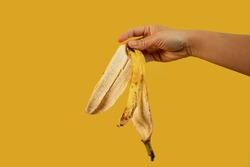 cropped view of man holding banana peel in hand isolated on yellow