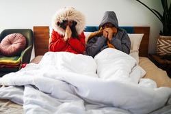 Couple cold on bed at home with winter coat in a blanket