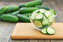 chopped fresh cucumber slices in a clear glass bowl on a wooden table, rustic style. Fresh cucumber. lot of cucumbers in a wooden bowl.