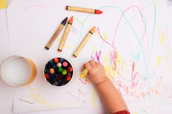 A hand of baby drawing lines and shapes with colorful crayons.