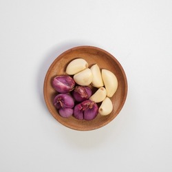 A wooden bowl with peeled garlic and red onion