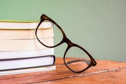 Books and glasses on a wooden table, on green background