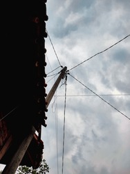 photo of an electricity pole close to the house, the sky is cloudy