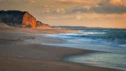 A vast and empty summer Atlantic beach in Portugal, in the warm light of the setting sun