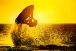 Silhouette of man drive freestyle jet ski at sunset.Professional rider do tricks in the sea.