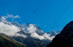 Base jumper in the distance is parachuting down to the valley in Lauterbrunnen in the Swiss Alps. Cloud covered mountains are visible in the background.
