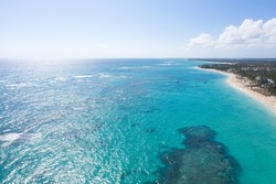 Bounty and pristine coastline with resorts, palm trees, caribbean sea and people having fun on beach. Travel destinations. Dominican Republic. Aerial view