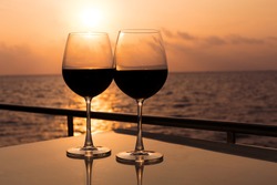 Romantic luxury evening on cruise yacht with winery setting. Glasses, red wine and tropical sunset with sea background, nobody. 