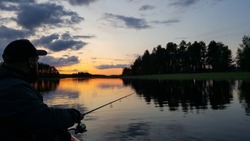 Fishing rod wheel closeup, man fishing with a beautiful sunrise/sunset behind him. Finland