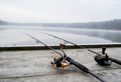 Fishing rod and wheels on the wooden pier, misty fog against the backdrop of lake. The concept of rural getaway. Article about fishing day.