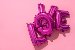 some fuchsia letter-shaped balloons forming the word love against a pink background, with a blank space on the left