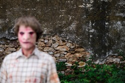 an intentionally unfocused scary disfigured man, wearing dirty and ragged clothes, in front of a ruined and abandonded house, the point where the focus is