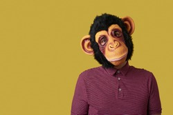 portrait of a man wearing a monkey mask on a yellow background with some blank space on the left