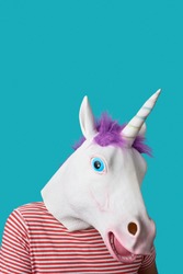 portrait of a man wearing a unicorn mask and a red and white striped t-shirt, on a blue background with some blank space on top