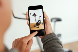 closeup of a young caucasian man taking a picture, with his smartphone, of a stationary bicycle to sell it on an online marketplace app to sell and buy secondhand goods