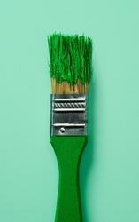 closeup of a green paintbrush with green pain, on a pale green background