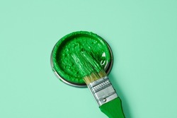 closeup of a paintbrush and the lid of a paint can with green pain, on a pale green background