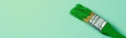 a green paintbrush with some green paint, on a pale green background with some blank space on the left, in a panoramic format to use as web banner or header