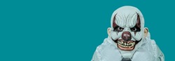 evil clown, wearing gloves and a costume with a white ruff, staring at the observer with a creepy smile, on a blue background with a blank space on the left, in a panoramic format to use as web banner