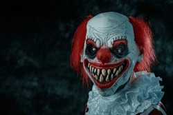 a mad evil redhead clown, wearing a white and red striped costume with a white ruff, stares at the observer with a creepy smile, in front of a dark background