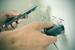 closeup of the hands of a man plugging in the plug of his smpartphone in a socket, with a filter effect