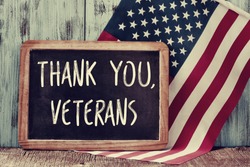 the text thank you veterans written in a chalkboard and a flag of the United States, on a rustic wooden background