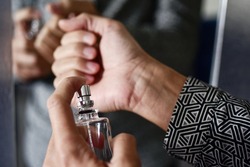 closeup of a young caucasian man spraying perfume on his wrists