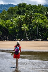 a lone girl with a backpack walks on a paradise tropical beach in marino ballena national park, Costa Rica; a panorama of a Costa Rican beach with palm trees and mountains in the background	