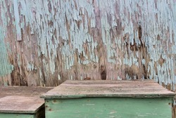 Paint chipped, weathered wood wall with wooden boxes in front of it. Aqua-green and aqua-blue paint chipping of and wood damp and rotting