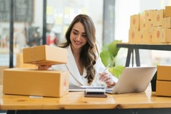 Happy young asian woman startup small business freelance holding parcel box and computer laptop and sitting on chair, Online marketing packing box delivery concept