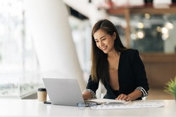 Cheerful business lady working on laptop in office, Asian happy beautiful businesswoman in formal suit work in workplace. Attractive female employee office worker smile.