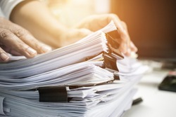 Work from Home, Businessman hands working in Stacks of paper files for searching information on work desk home office, business report papers,piles of unfinished documents achieves with clips indoor.