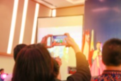 Blur of woman hands take photo or recording speaker with smart phone, camcorder mobile operator working for record speaker on stage in conference and convention hall 